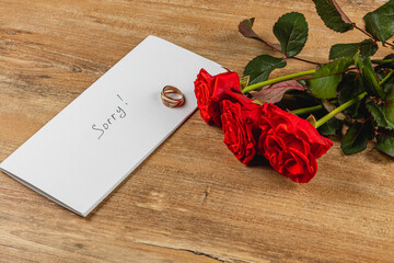 Broken engagement letter with roses and wedding ring on wooden table