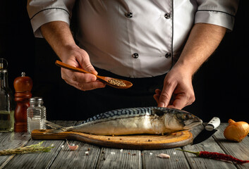 A chef is seasoning a fresh mackerel fish using a wooden spoon to sprinkle spices. The rustic...