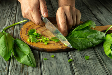 A pair of hands skillfully chop fresh green herbs on a wooden board. The kitchen atmosphere is warm and inviting, emphasizing home cooking