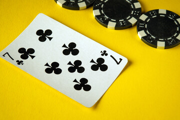 Seven of clubs card placed on a vibrant yellow surface alongside several black casino chips,...