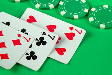 Green chips and playing cards with a combination of three of a kind or set are randomly laid out on a poker table. The concept of a lucky win in a club