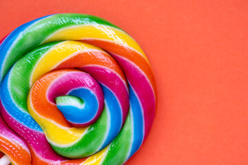 Detailed macro of colorful swirl lollipop on bright orange surface. High contrast candy photo...