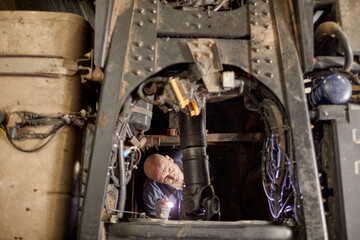 Man inspecting complex machinery in industrial setting, holding flashlight for better visibility. Detailing mechanical parts and working environment, emphasizing maintenance process