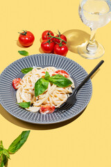 Creamy spaghetti with cherry tomatoes, cheese and basil on a plate on a yellow background