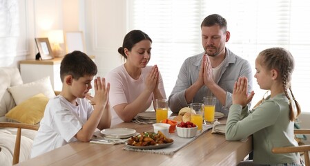Family praying together before dinner at table indoors
