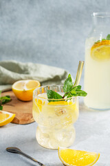 Fresh drink lemonade with lemon, mint and ice in glass on a light background with bottle