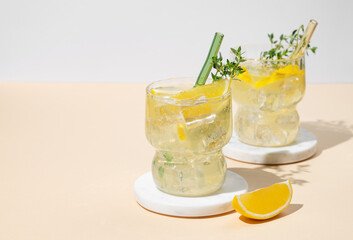 Two glasses of fresh drink lemonade with lemon, thyme and ice on a yellow background with shadows.
