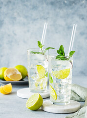 Two glasses mojito cocktail with fresh lime, mint and ice on a marble stand on blue texture background.