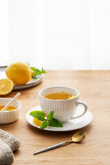 Cup of herbal tea with lemon, honey and mint on wooden tabletop with citrus fruits