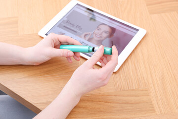 Beauty blogger holding mascara at wooden table with tablet indoors, closeup