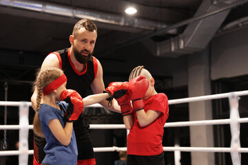 Children practicing fight on boxing ring under their coach supervision