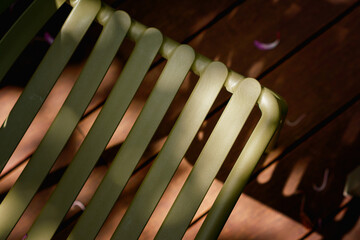 Abstract minimalist design of an olive green slatted outdoor chair surface. Dappled sunlight creates strong contrasts and highlights its smooth texture, evoking calm outdoor relaxation.