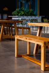 Clean lines of modern wooden benches and tables in a contemporary cafe or eatery. Warm wood tones contrast with cool polished concrete floors, creating an inviting, minimalist interior space.