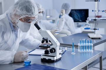 Scientist in protective suit working with microscope at laboratory