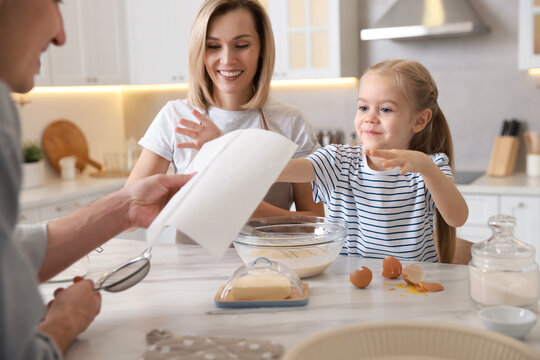Happy parents and their daughter making dough at white marble table in kitchen