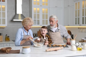 Grandparents and their grandson cooking together at white marble table in kitchen