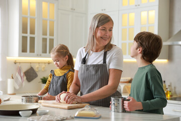 Grandmother and her grandchildren making dough at white marble table in kitchen