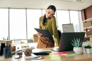 Young businesswoman working in modern office planning a project with documents and laptop, discussing ideas over phone