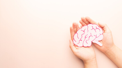 Woman hands holding human brain shape made from paper on beige background. Awareness of Alzheimer,...