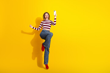 Young woman in trendy casual outfit celebrates joyfully against vibrant yellow background