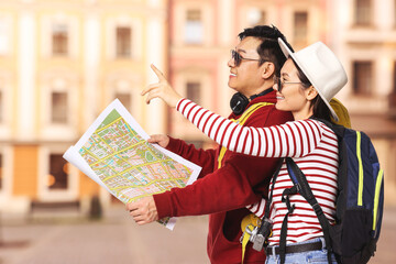 Happy tourists with map pointing at something on city street