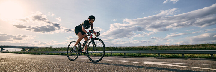 Wide angle view photo of cyclist on open highway, riding under dramatic sky with bridge in distance...
