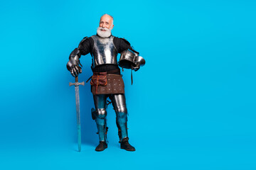 Naklejka premium Elderly Man Dressed as a Medieval Knight Holding Sword Against Blue Background