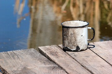 Naklejka premium Old metal cup on a weathered wooden pier by the calm water