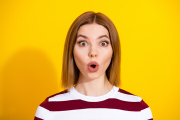 Surprised young woman in striped sweater expressing surprise, isolated on vibrant yellow background