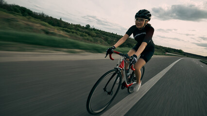 Fototapeta premium Motion blur photo of cyclist speeding through countryside, strong pedaling movement, concentration on face, asphalt blurred into horizon. Concept of velocity, drive, strength, competition.
