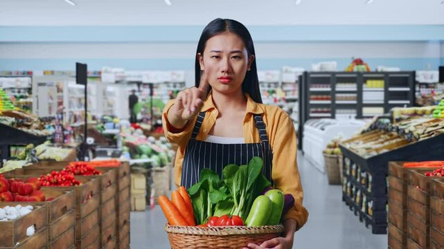 Asian Female Farmer With Vegetable Basket Showing Stop One Finger Gesture, Taboo Sign in Grocery Store