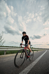 Confident girl, cyclist in full gear riding along open countryside road, powerful stride and focused eyes locked on route ahead. Concept of commitment, sport, movement, fitness journey.