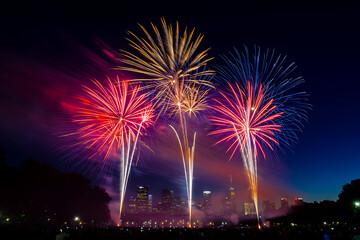 Spectacular fireworks illuminate the night sky above the city, creating a vibrant display of red, white, and gold against the dark backdrop