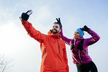 A cheerful couple take a light hearted selfie on a mountain summit, celebrating their hike with fun gestures.