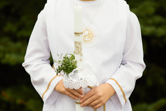 Young child in white communion robe holding a decorated candle during First Holy Communion. Polish Catholic tradition celebrating faith, purity, and spiritual growth.