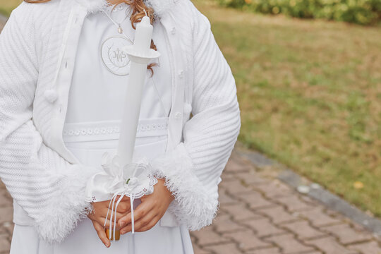 Young child in white communion robe holding a decorated candle during First Holy Communion. Polish Catholic tradition celebrating faith, purity, and spiritual growth.