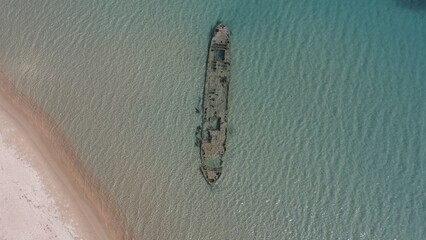 Aerial beach view with old shipwreck in green sea
