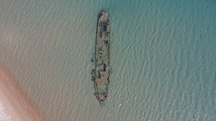 Aerial beach view with old shipwreck in green sea
