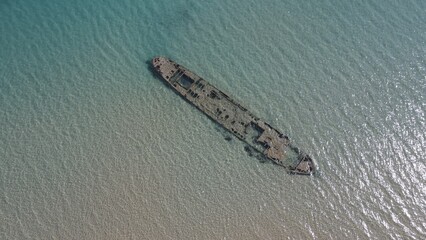 Aerial beach view with old shipwreck in green sea
