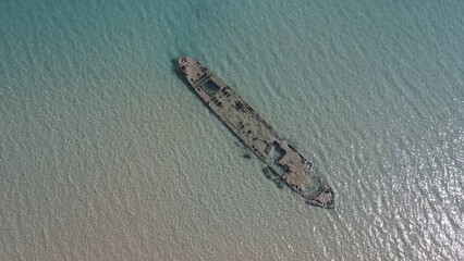 Aerial beach view with old shipwreck in green sea
