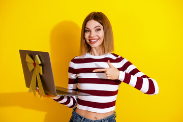 Smiling young woman in stylish striped top holding a gifted laptop with a gold bow on vibrant...