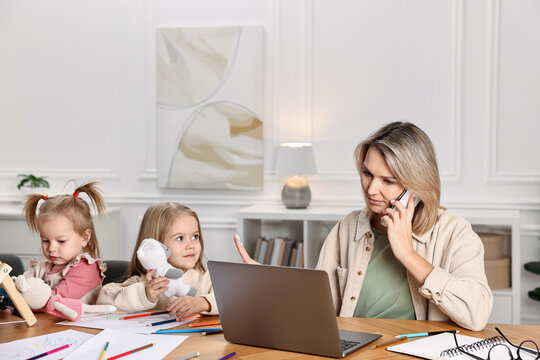 Work-family balance. Single mother talking by smartphone and refusing to play with her children at wooden table indoors