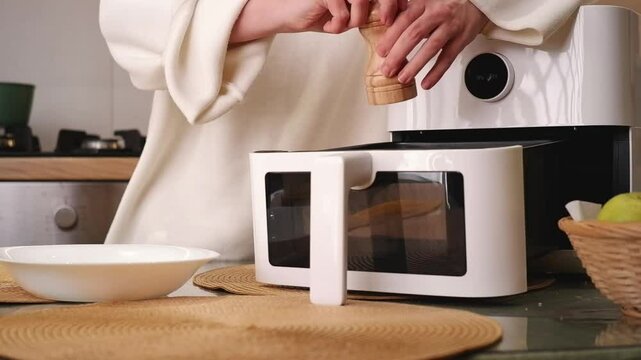 Woman preparing and cooking corn on the cob in an air fryer in a domestic kitchen