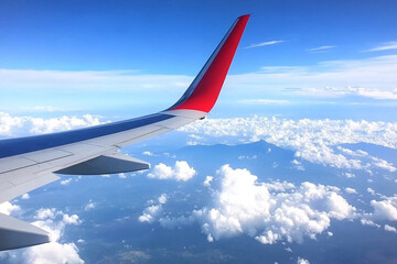 Airplane wing with red tail fin against a backdrop of blue sky and fluffy white clouds