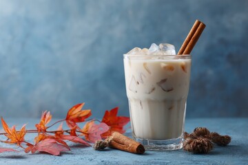 Autumnal Iced Chai Latte Still Life: Refreshing Drink with Cinnamon Sticks and Fall Leaves on Blue Textured Surface