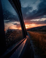 Car window with raindrops at sunset on road trip travel adventure in countryside landscape golden hour cinematic view