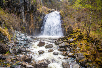 Korbu waterfall near Teletskoye lake in Altai Russia. Powerful stream of water falling from cliff surrounded by wild forest