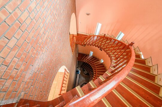 high-angle shot of a spiral staircase in a building with peach-colored walls. The stairs are wooden with decorative accents. - Powered by Adobe