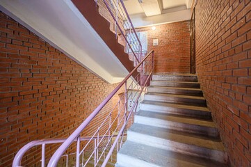 Fototapeta premium stairwell with brick walls and a pink metal railing. Concrete stairs lead upwards