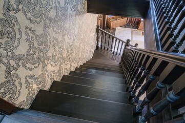 Obraz premium high-angle shot of a dark wooden staircase descending. An ornate patterned wallpaper adorns the adjacent wall, offering a contrast to the staircase